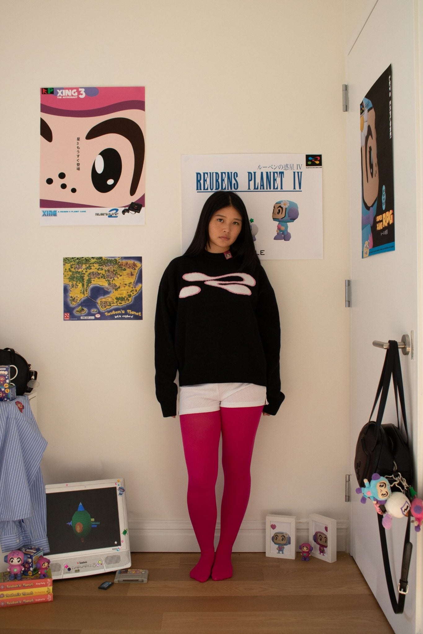 Person wearing a black sweater with a white design and pink tights standing in a room with posters on the wall.
