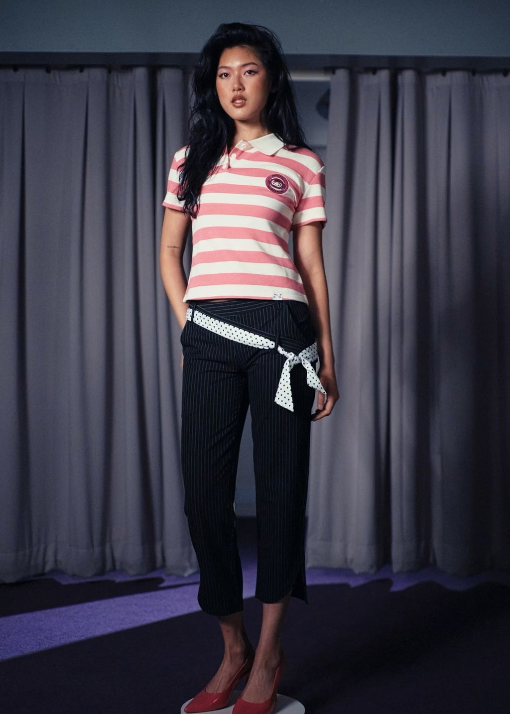 Woman wearing a striped shirt and black pants standing against a plain background